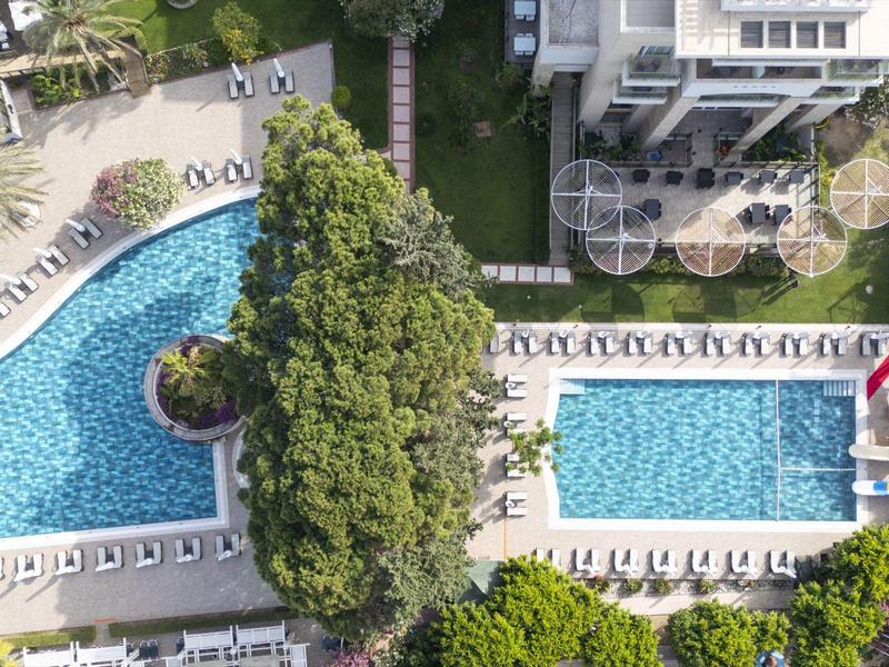 Vue aérienne d'un hôtel avec deux grandes piscines entourées de chaises longues et d'arbres.