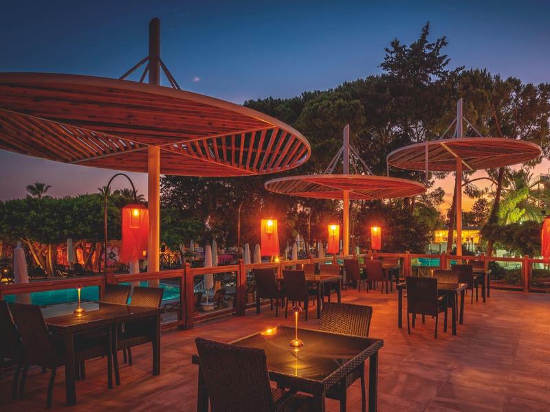 Terrasse d'hôtel au crépuscule avec parasols ronds et chaises éclairées par une lumière chaude.