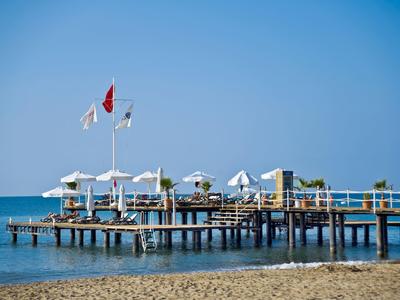 Houten pier met witte parasols en vlaggen die uitsteekt over kalme zee onder een heldere blauwe lucht.