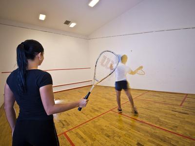 Due donne giocano a squash in un campo da squash luminoso con pavimento in legno.