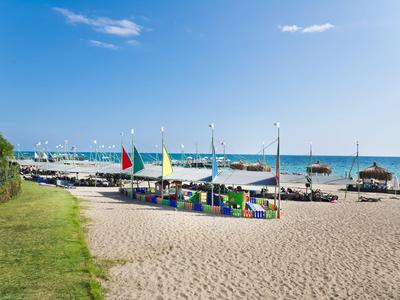 Spiaggia sabbiosa con sedie a sdraio colorate e bandiere sotto un cielo azzurro vicino al mare.
