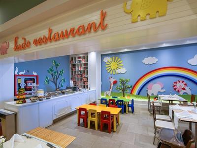 Kleurrijk kinderrestaurant met kleine tafels, stoelen en speelse muurschilderingen zoals een regenboog.