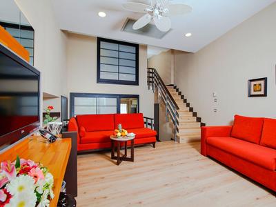 Gezellige woonkamer met rode banken, houten vloer, tv en trap naar boven.