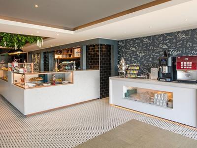 Moderne hotelcafe met glazen toonbanken, koffiemachine en groene decoratie boven.