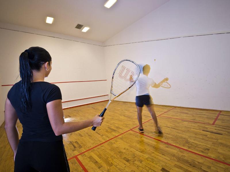 Twee vrouwen spelen squash in een binnenbaan met houten vloeren en witte muren.