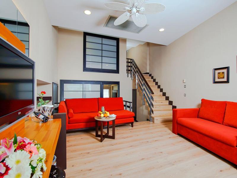 Gezellige woonkamer met rode banken, houten vloer, tv en trap naar boven.