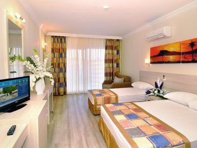 Brightly furnished hotel room with two beds, TV, and a balcony with curtains.