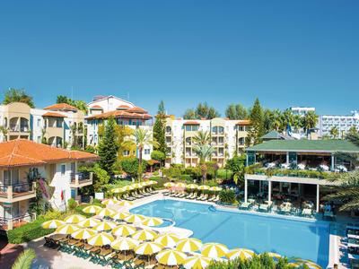 View of a resort with pool, sun umbrellas, and surrounding buildings under a blue sky.