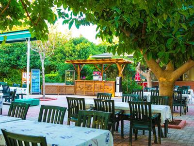 Außenbereich eines Cafés mit Tischen, Stühlen und Bäumen bei sonnigem Wetter.
