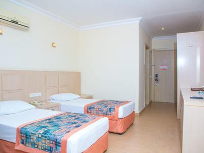 Zimmer mit zwei Einzelbetten, weißen Wänden, Ventilator, TV und einfachem, sauberem Design.