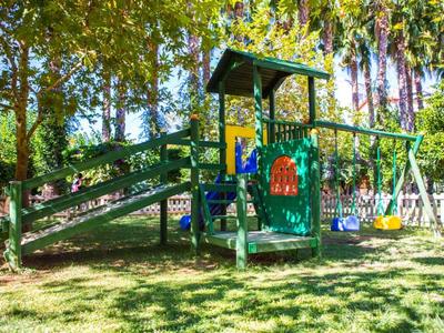 Bunte Kinderspiellandschaft mit Rutsche, Klettergerüst und zwei Schaukeln im grünen Garten.