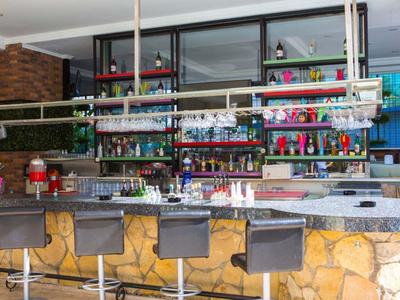 Moderne Bar mit grauen Barhockern, heller Steinverkleidung und bunten Flaschenregalen im Hintergrund.