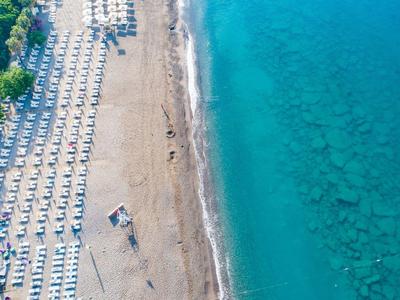 Luftaufnahme eines Sandstrands mit Reihen von Sonnenschirmen und Liegestühlen neben klarem, blauem Meer.