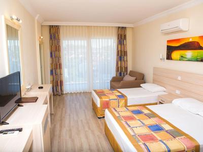 Helles Hotelzimmer mit zwei Betten, Fernseher, Sofa, Klimaanlage und großen Fenstern mit Vorhängen.