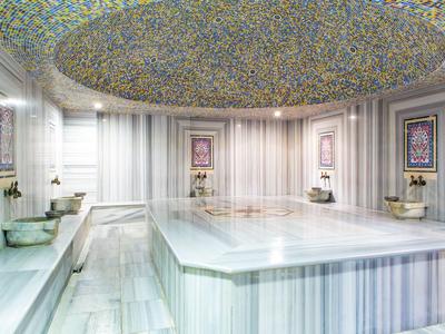 Heller, großer Hamam mit Marmorwänden, zentralem Becken und farbenfroher Deckenmosaik.