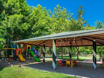 Covered outdoor area and colorful playground next to green trees and blue sky.