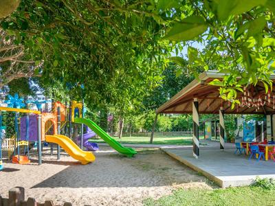 Children's playground with slide and seating area under trees at a hotel facility.
