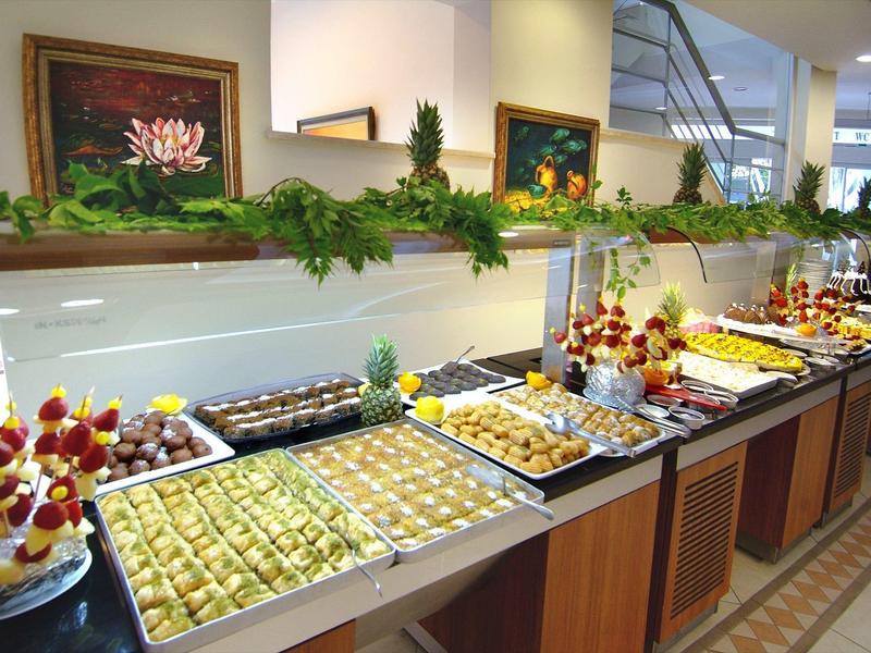 Buffet mit verschiedenen Süßspeisen, Dekoration aus grünen Blättern und roten Blumen.