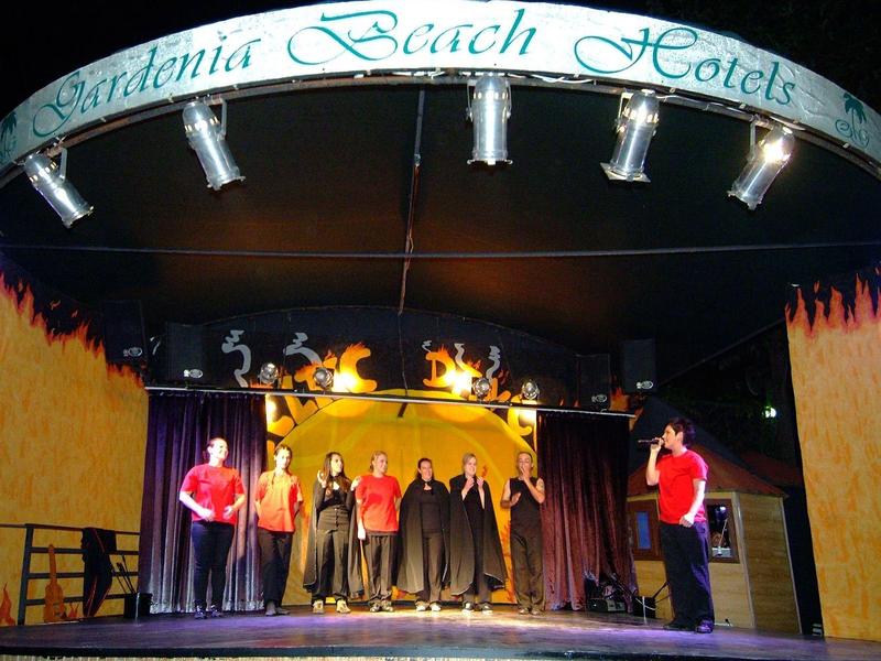 Bühne mit zehn Menschen, darunter Sprecher vor Mikrofon, unter grünem ?Sardinia Beach Hotels?-Schild.