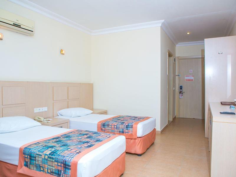 Zimmer mit zwei Einzelbetten, weißen Wänden, Ventilator, TV und einfachem, sauberem Design.