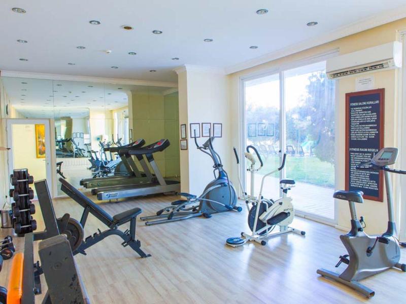 Heller Fitnessraum mit Hanteln, Laufband, Fahrradergometer und großem Fenster mit Gartenblick.