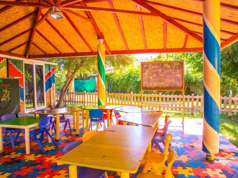 Buntes, überdachtes Kinderspielzimmer mit kleinen Tischen, Stühlen und Spielzeug in lebendigen Farben.