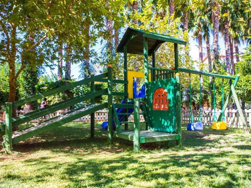 Bunte Kinderspiellandschaft mit Rutsche, Klettergerüst und zwei Schaukeln im grünen Garten.