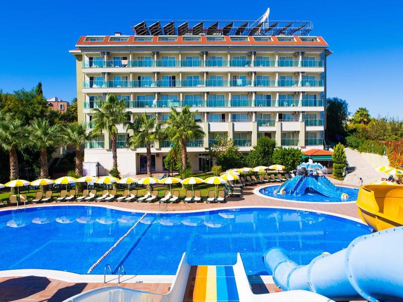 Hotel mit großem Schwimmbad, Wasserrutschen, Sonnenliegen und Palmen unter klarem blauem Himmel.