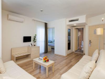 Heller Wohnraum mit beigen Sofas, kleinem Tisch, Fernseher und kühlender Klimaanlage an der Wand.