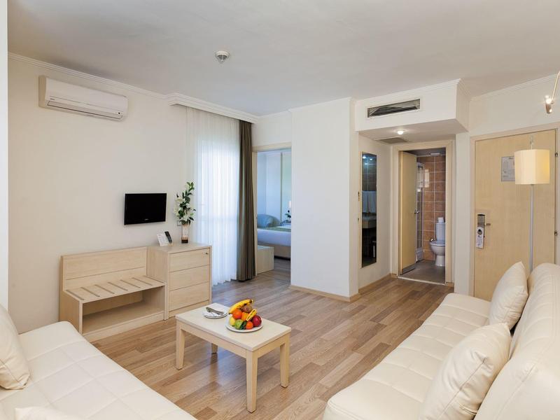 Modern, bright living area with two sofas, coffee table, and TV in a hotel room.