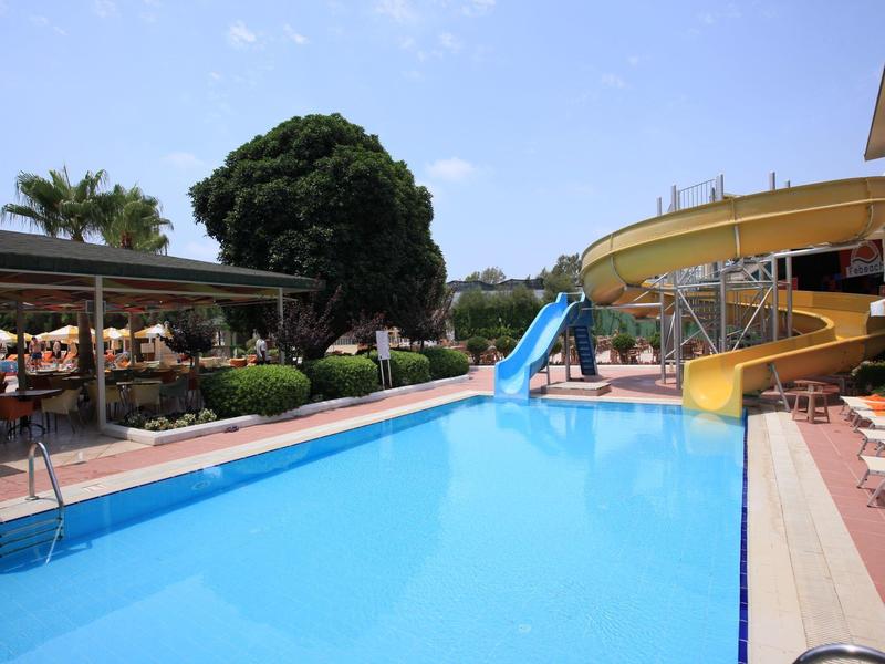 View of a clear blue pool with water slides and lounge chairs on a sunny day.