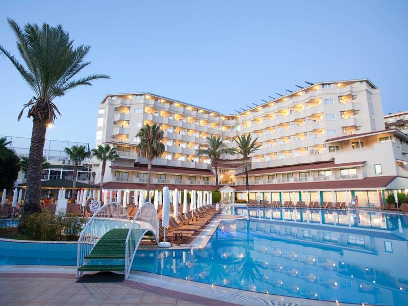 Large hotel with illuminated pool, palm trees, and sun loungers at dusk.
