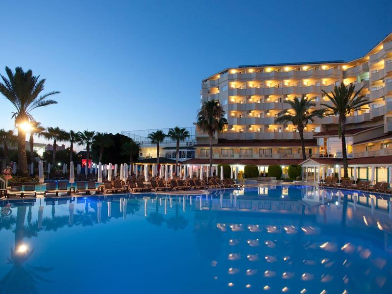 Large hotel with illuminated pool and palm trees at sunset