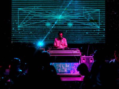 DJ suona musica davanti a uno schermo luminoso in un club buio con persone che ballano.