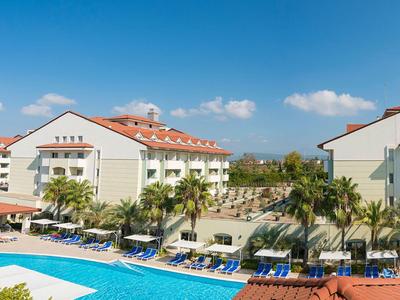 Resort with a large pool, lounge chairs, palm trees, and modern white buildings under a clear sky.