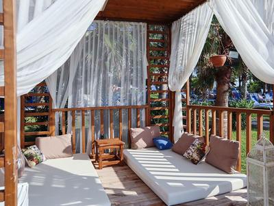 Cozy wooden outdoor lounge with white drapes, cushions, and a small rocking chair under a shaded patio.