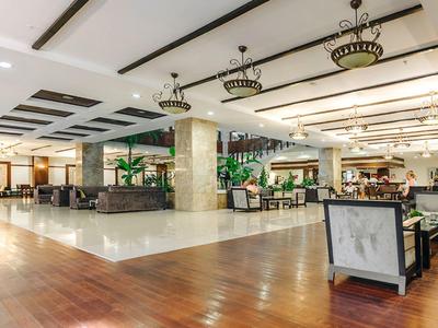 Spacious hotel lobby with seating areas, decorative lighting, and mix of wooden and tiled flooring.