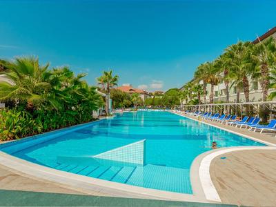 Outdoor pool with sunbeds and palm trees at a resort under a clear blue sky.