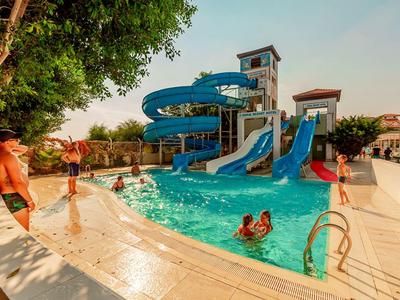 Outdoor pool with blue water slides, surrounded by sunbathers and children playing in water.
