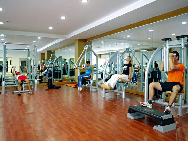 Indoor gym with wooden floor, multiple exercise machines, and people working out.