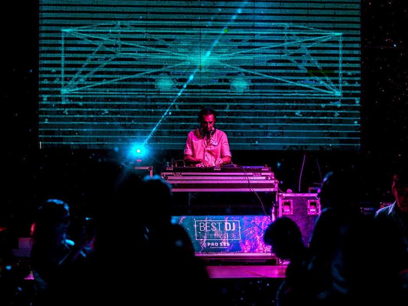 DJ performing with colorful light effects in a dim nightclub setting.