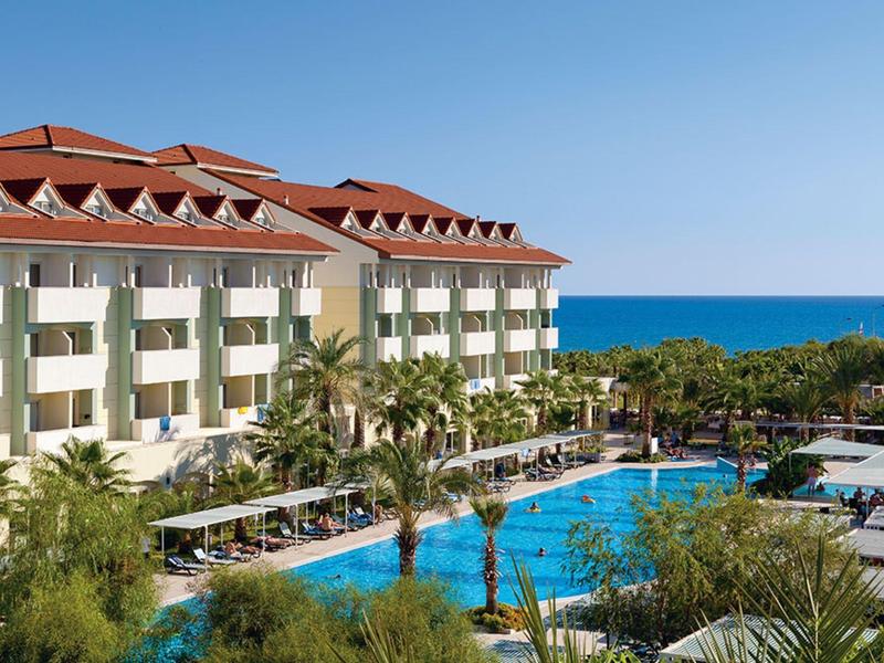 Resort hotel with large pool, palm trees, and sea view on a sunny day.