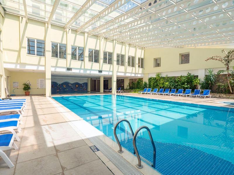 Indoor hotel swimming pool with lounge chairs and large glass ceiling.