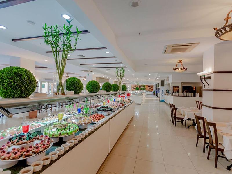 Spacious hotel dining area with buffet table featuring desserts and green floral decorations.
