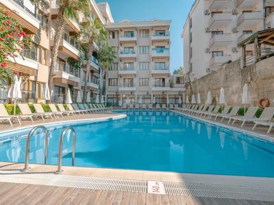 Grande piscina esterna con lettini tra due edifici pluripiano sotto un cielo azzurro.