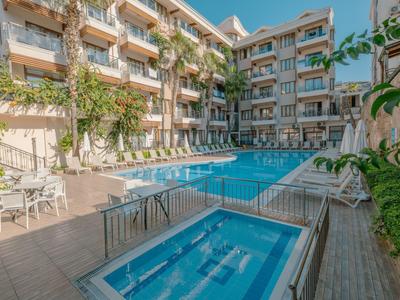 Edificio dell'hotel con piscina all'aperto e vasca idromassaggio, circondato da lettini e piante.