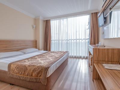 Camera d'hotel moderna con letto matrimoniale, mobili in legno e grande finestra con tende bianche