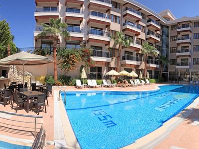 Großes Hotel mit blauem Pool, Sonnenliegen und Außenessbereich bei klarem Himmel.