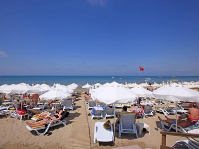 Spiaggia con lettini e ombrelloni bianchi, cielo azzurro e mare calmo.