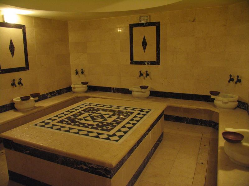 Tradizionale hammam turco con piattaforma centrale in pietra e lavandini lungo le pareti.